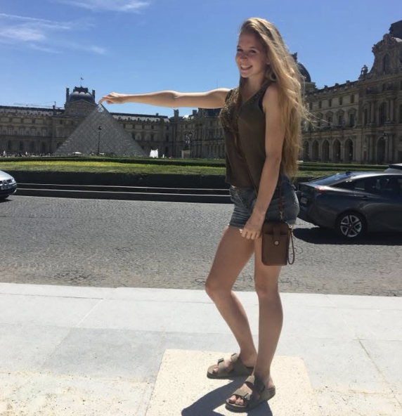 Girl posing in front of the triangle outdoor artwork at the Louvre